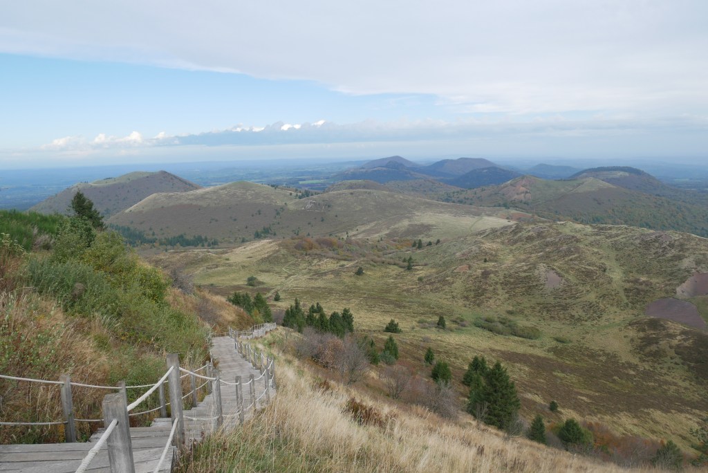 escalier en bois descendant au premier plan
plusieurs volcans de la chaine des puys en fond
